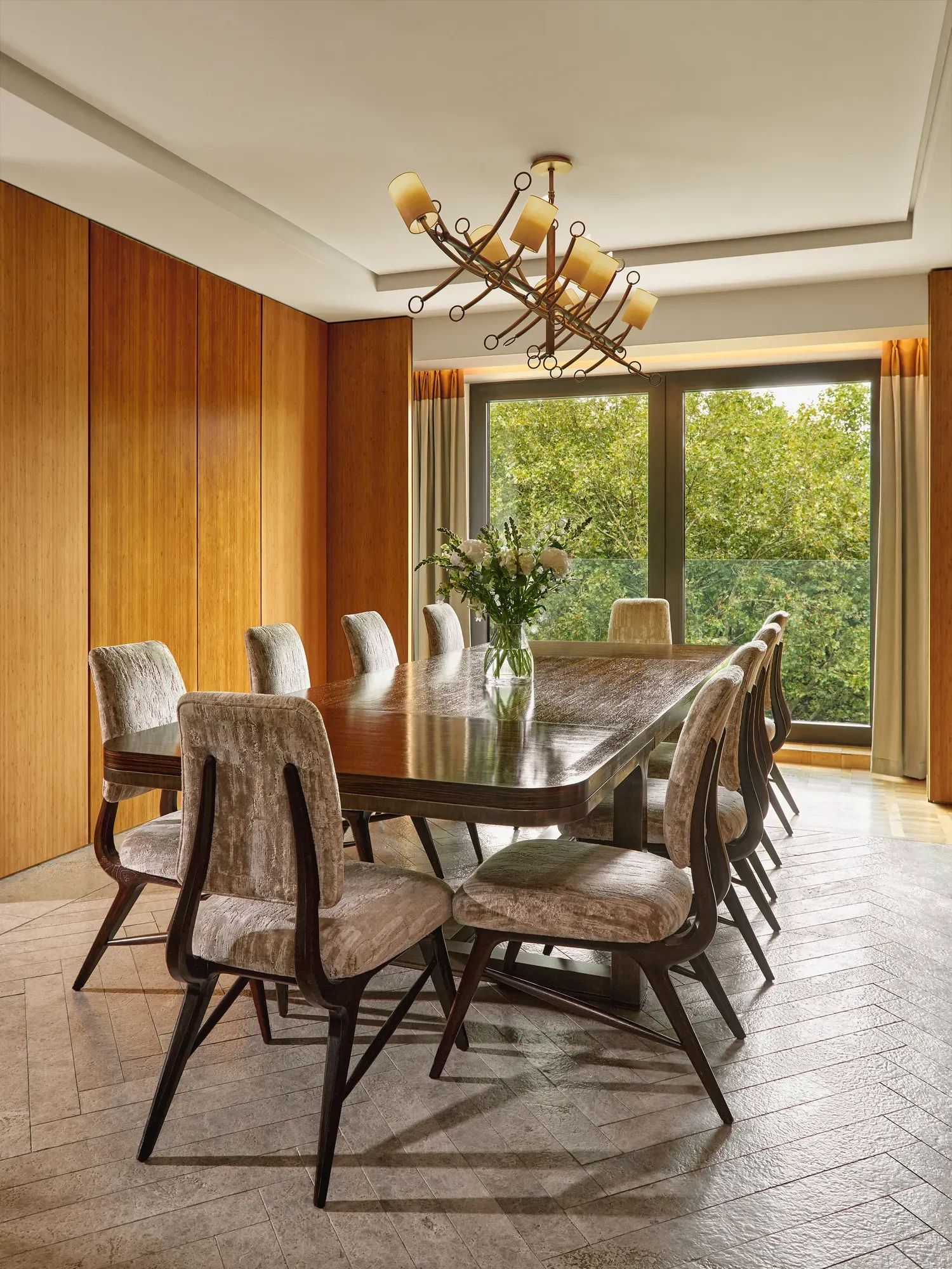 Opus Suite dining room with long wooden table, eight chairs, and large windows overlooking greenery