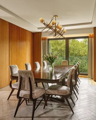 Opus Suite dining room with long wooden table, eight chairs, and large windows overlooking greenery