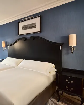 Elegant guest room with twin beds, blue walls, armchairs by window, and bedside tables.