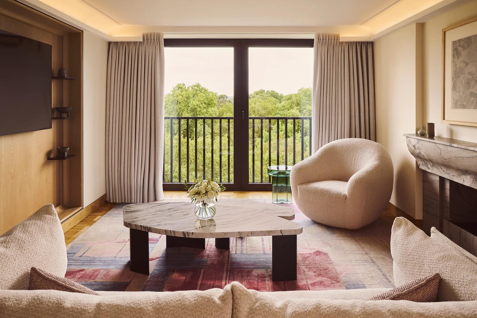 Bright living room with sofa, marble coffee table, armchair, and balcony doors overlooking trees.