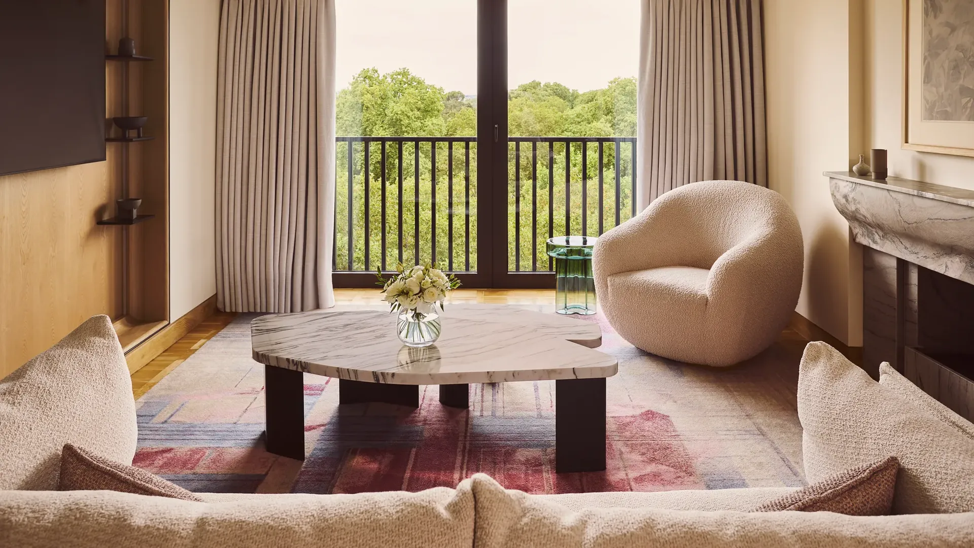 Bright living room with sofa, marble coffee table, armchair, and balcony doors overlooking trees.