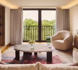 Bright living room with sofa, marble coffee table, armchair, and balcony doors overlooking trees.