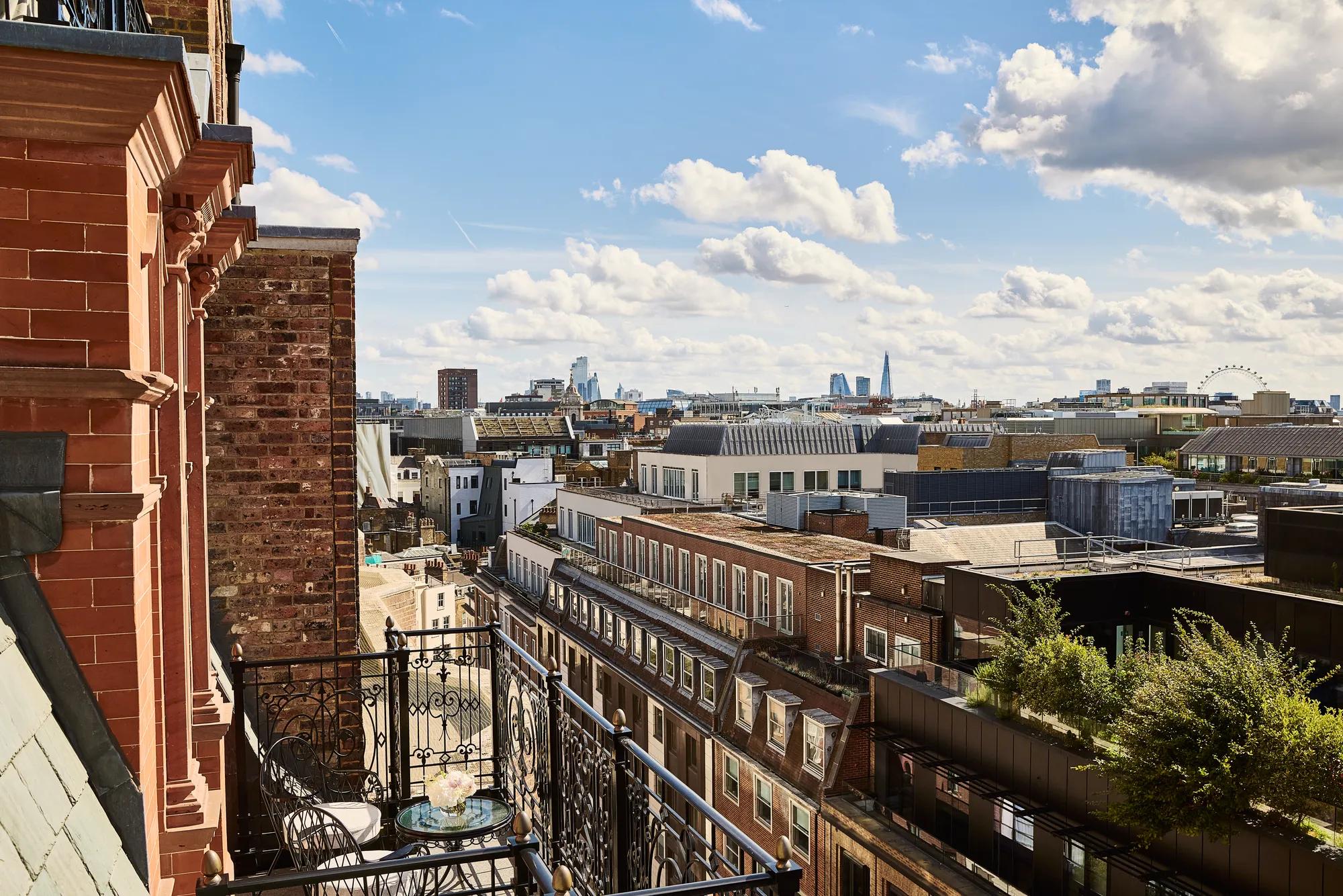 Wrought-iron balcony with table overlooking Mayfair rooftops and the London skyline beneath a bright sky.