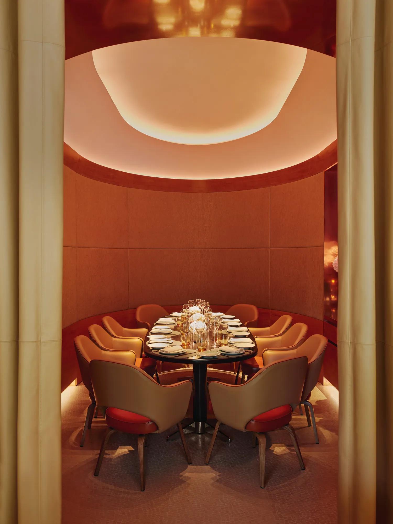 Curved private dining room with orange chairs, floral centerpiece, and soft ambient lighting.