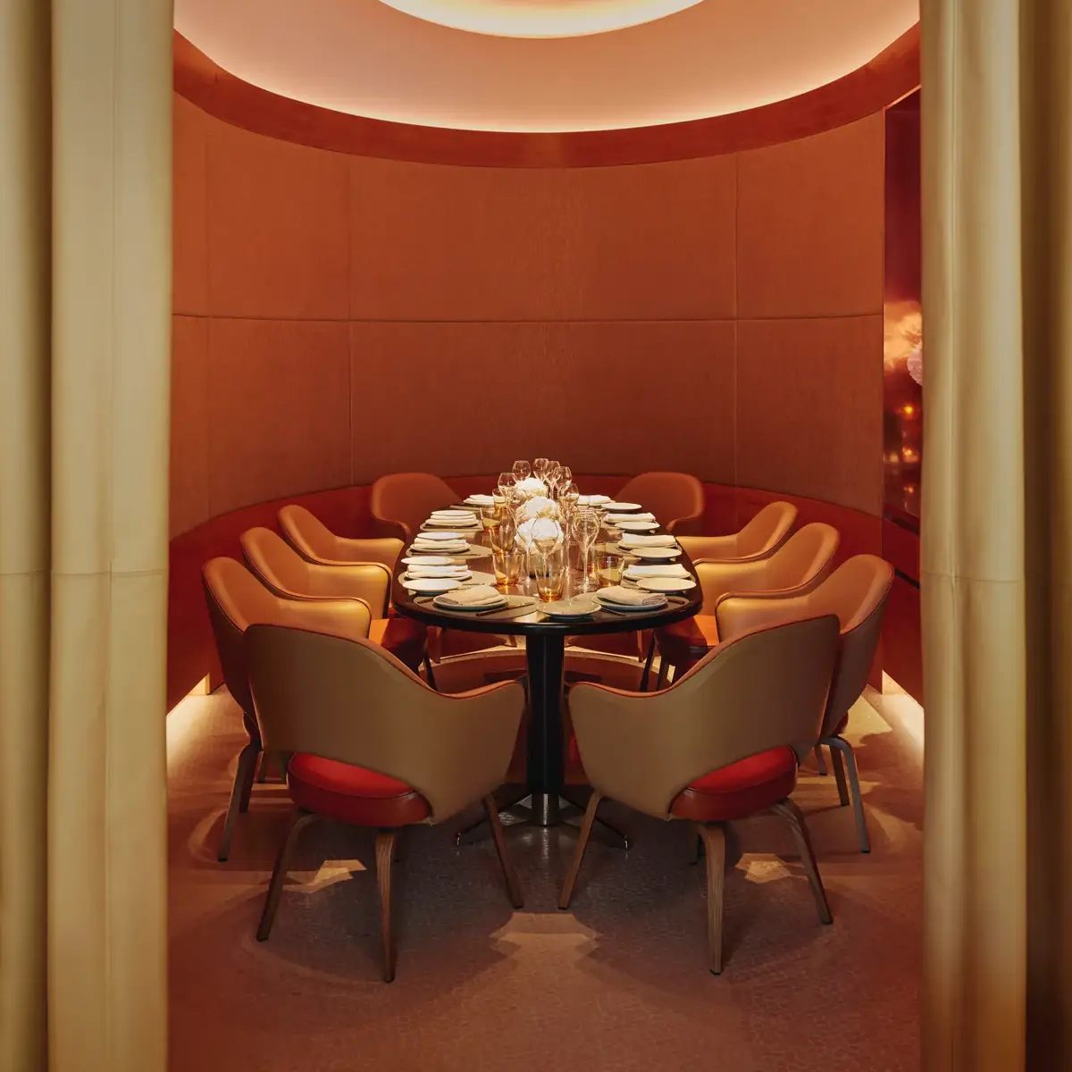 Curved private dining room with orange chairs, floral centerpiece, and soft ambient lighting.