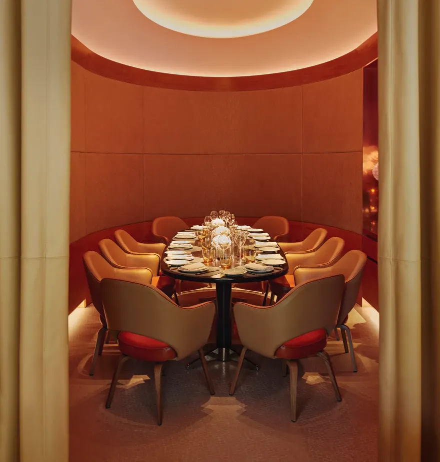 Curved private dining room with orange chairs, floral centerpiece, and soft ambient lighting.