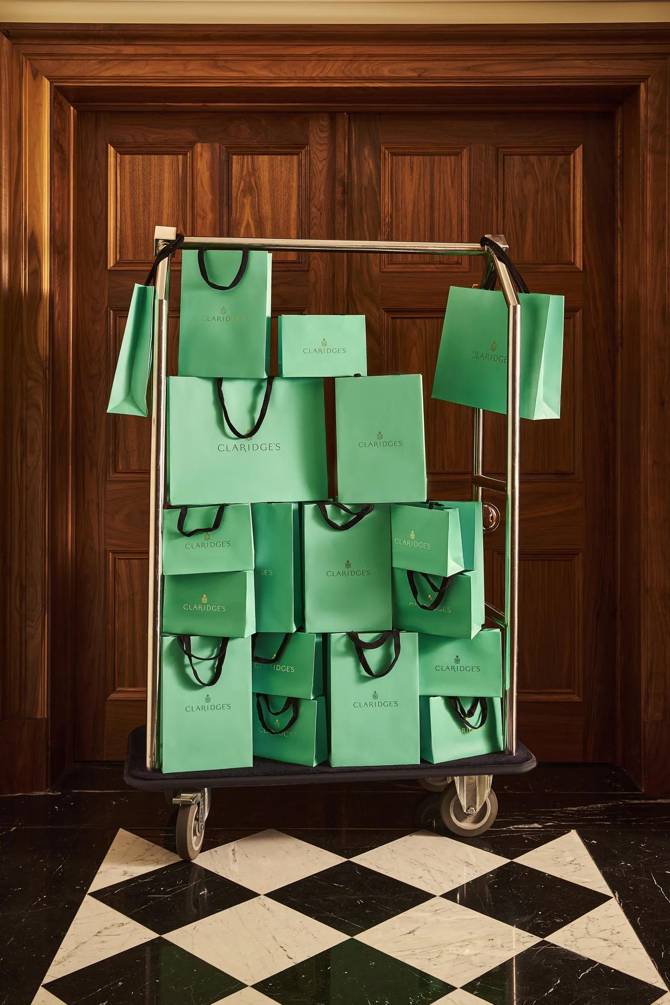 Claridge’s signature green shopping bags displayed on a luggage trolley against dark wood panelling.