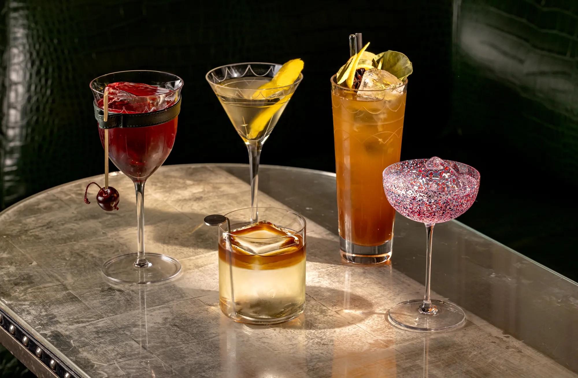Assortment of five cocktails in various glassware, with ice, straws, and fresh fruit accents.