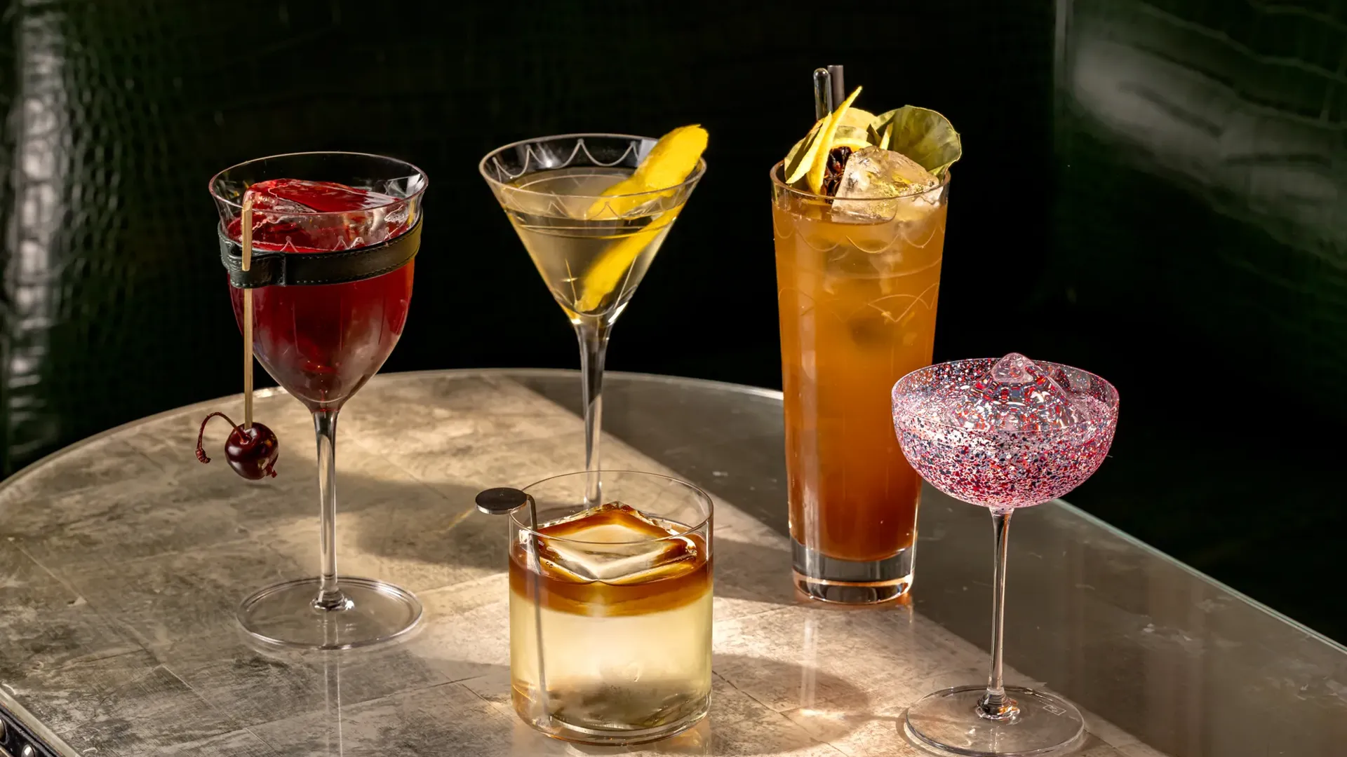 Assortment of five cocktails in various glassware, with ice, straws, and fresh fruit accents.