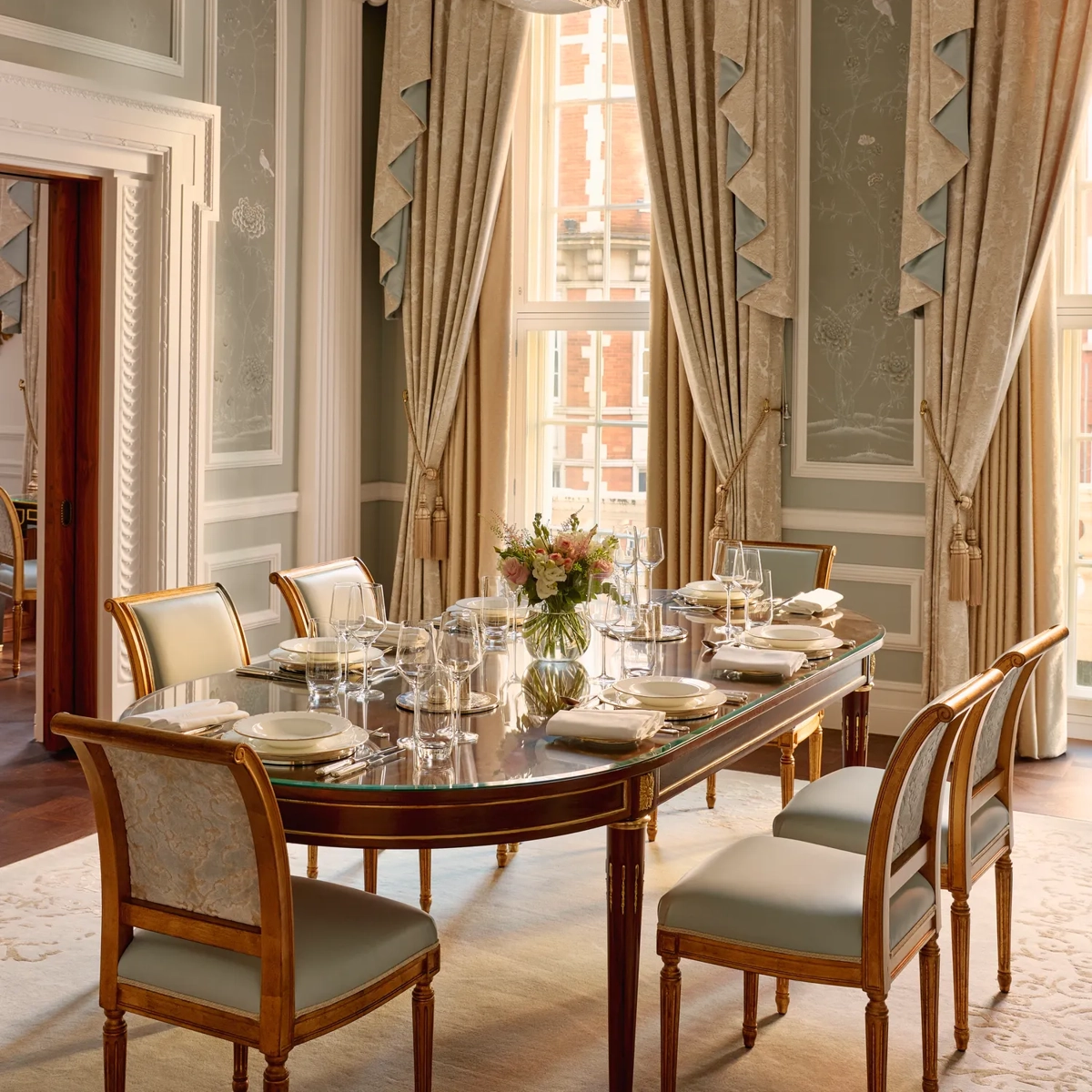 Elegant private dining room with chandelier, long table, and tall draped windows.