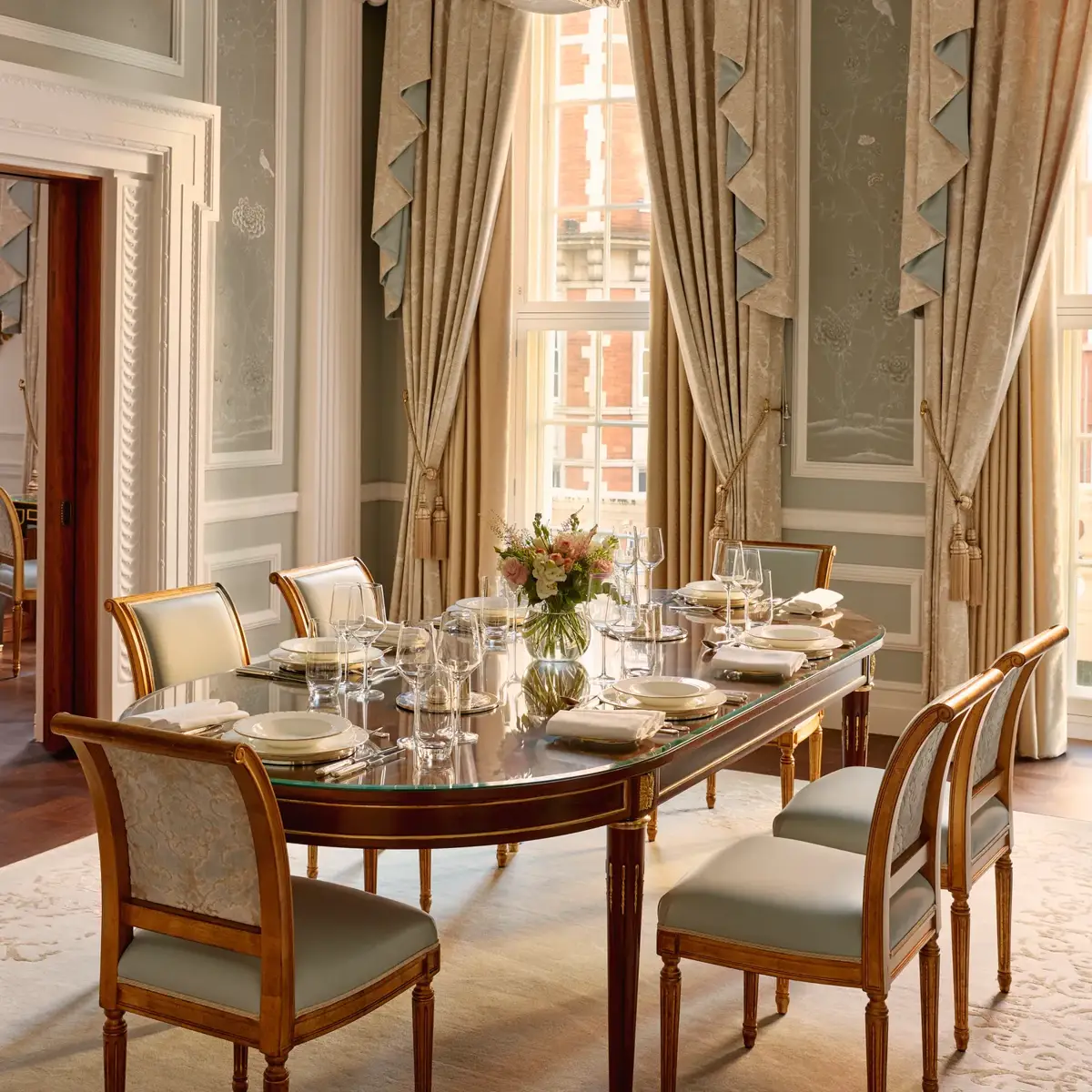 Elegant private dining room with chandelier, long table, and tall draped windows.