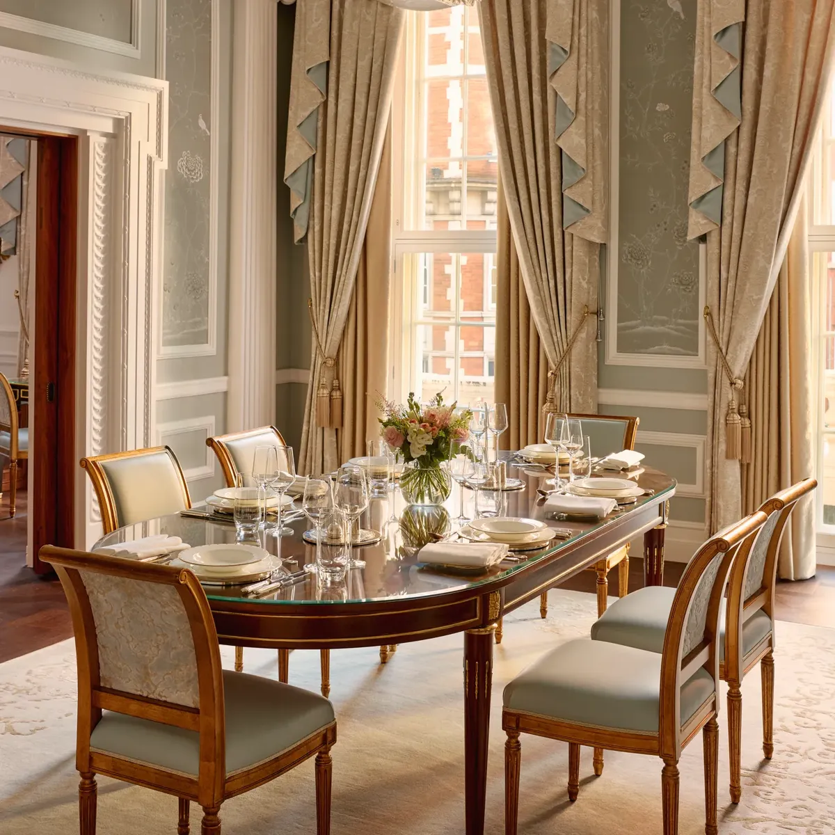 Elegant private dining room with chandelier, long table, and tall draped windows.