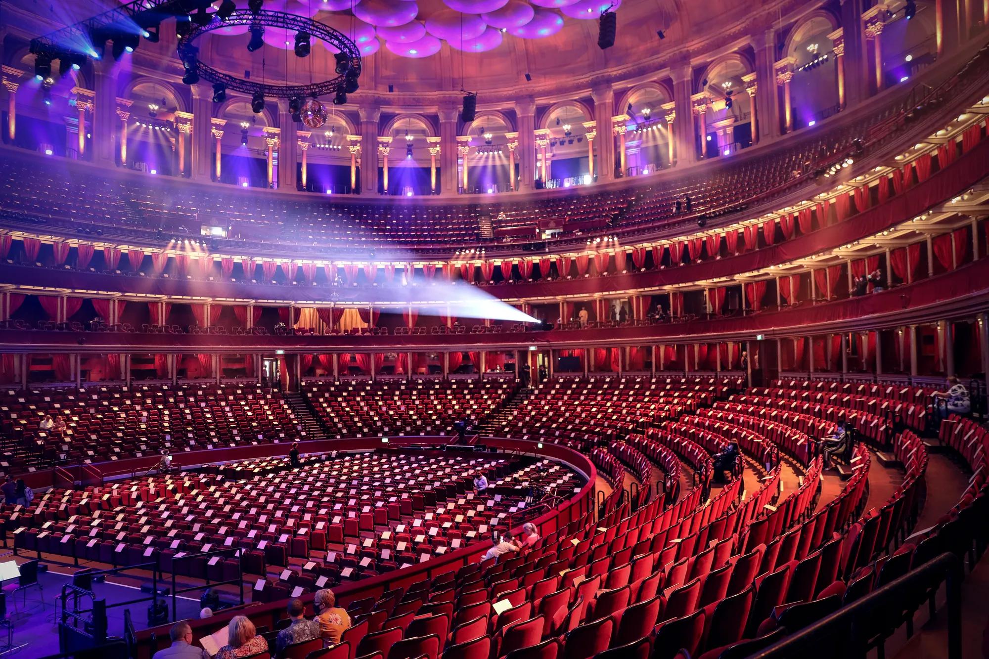 Grand circular concert hall interior with empty red seats and beams of stage lighting.