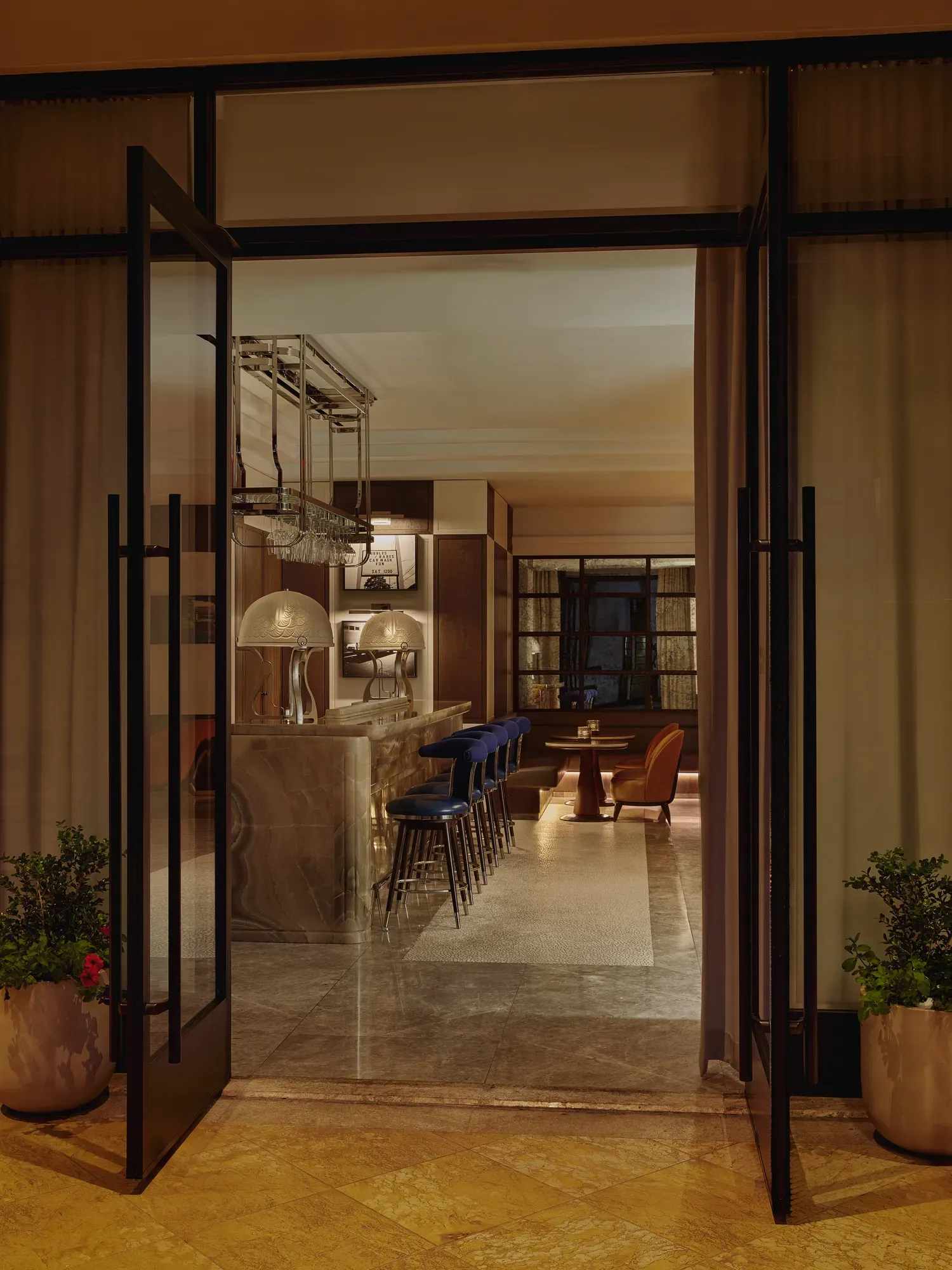 Open glass doors to an onyx bar with blue stools, mirrored back bar, and hanging glass racks.