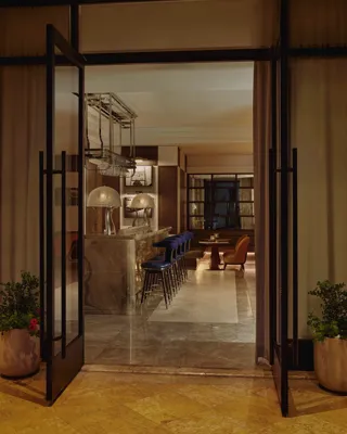 Open glass doors to an onyx bar with blue stools, mirrored back bar, and hanging glass racks.