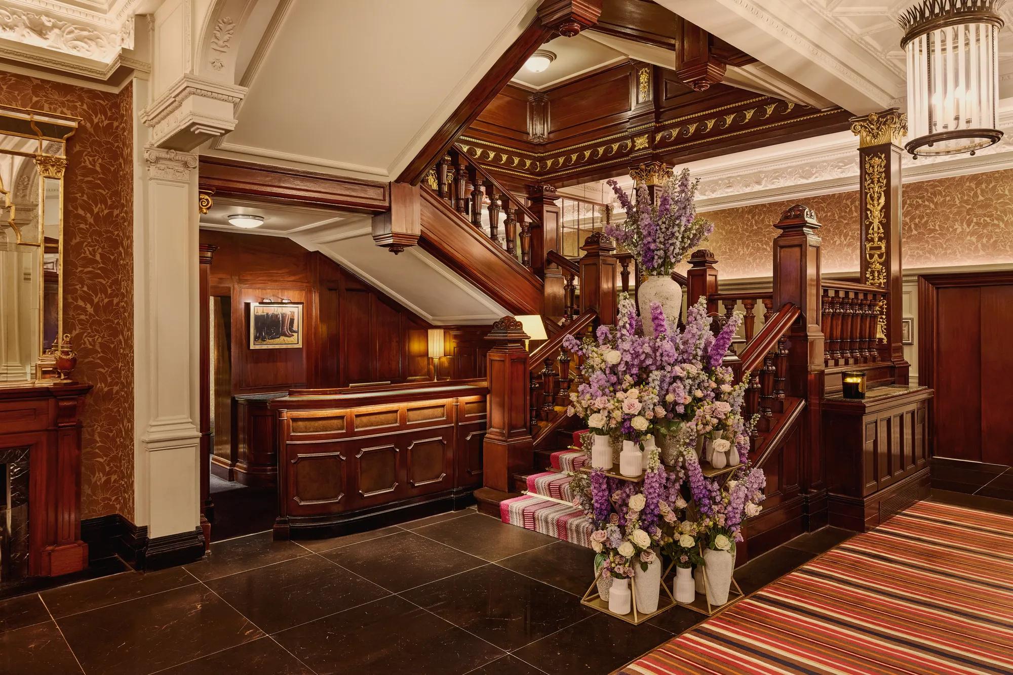 Elegant hotel staircase with dark wood panelling and a large floral arrangement in soft purple and cream tones.