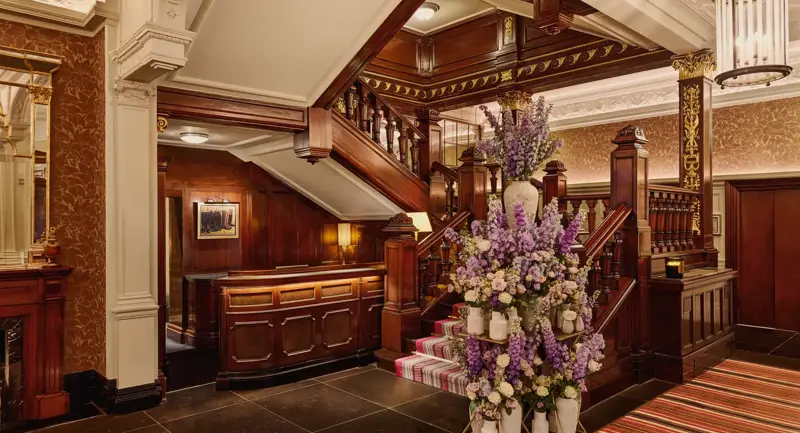 Elegant hotel staircase with dark wood panelling and a large floral arrangement in soft purple and cream tones.
