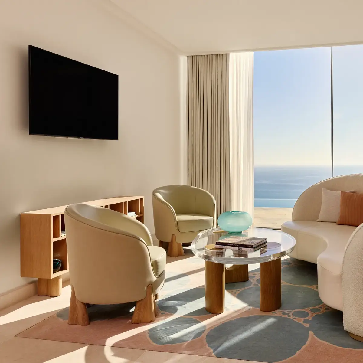 Salon lumineux avec canapé moderne incurvé, fauteuils et table basse en verre, donnant sur une vue panoramique de la mer.