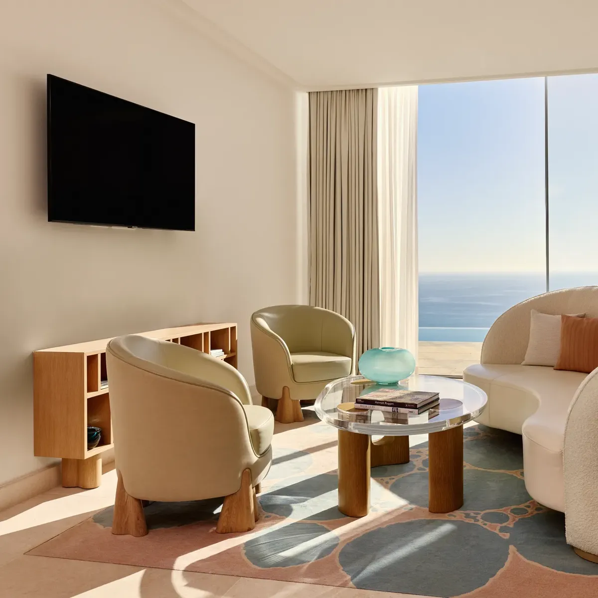 Salon lumineux avec canapé moderne incurvé, fauteuils et table basse en verre, donnant sur une vue panoramique de la mer.