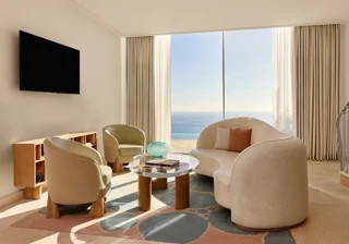 Bright living room with modern curved sofa, armchairs, and a glass coffee table, opening to a panoramic sea view.