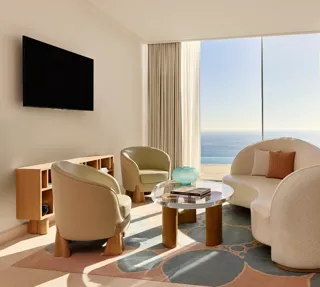 Salon lumineux avec canapé moderne incurvé, fauteuils et table basse en verre, donnant sur une vue panoramique de la mer.