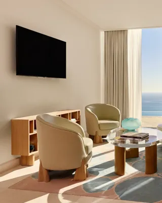 Salon lumineux avec canapé moderne incurvé, fauteuils et table basse en verre, donnant sur une vue panoramique de la mer.