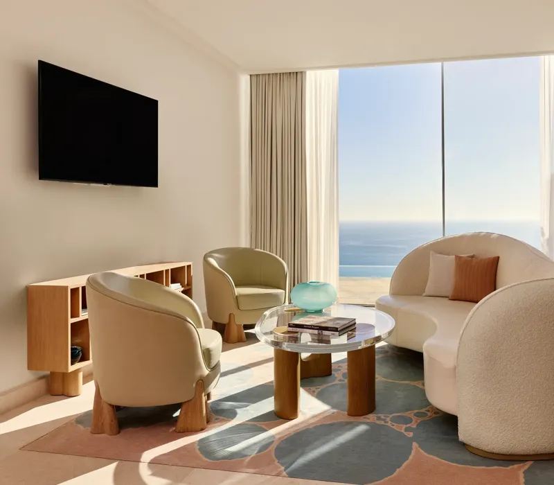 Salon lumineux avec canapé moderne incurvé, fauteuils et table basse en verre, donnant sur une vue panoramique de la mer.