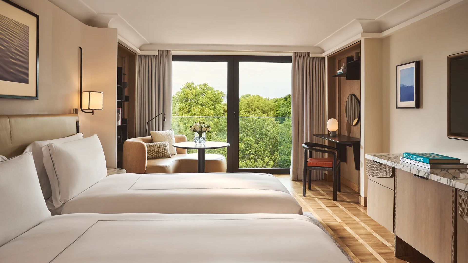 Modern bedroom with two twin beds and a sofa with orange pillows, large window overlooking green trees