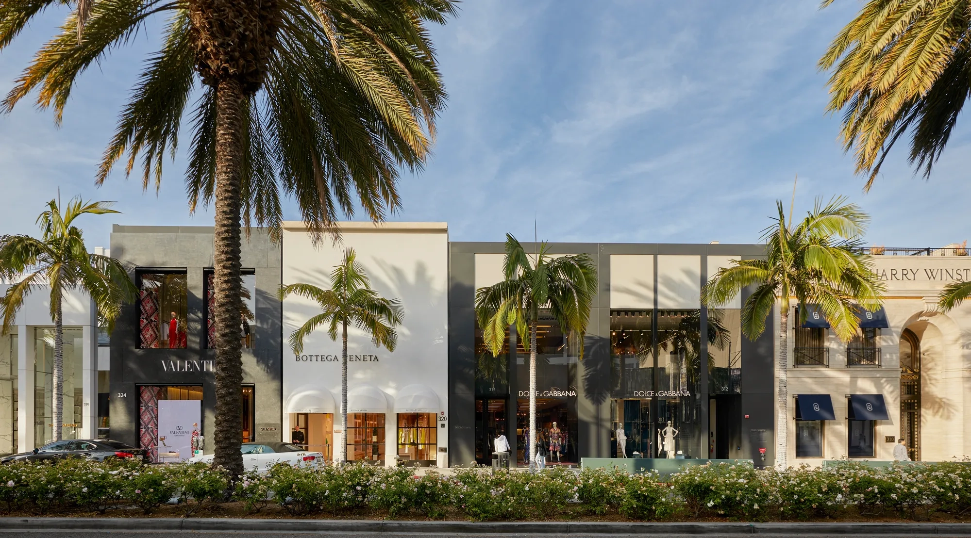 Rodeo Drive luxury storefronts—Valentino, Bottega Veneta, and Dolce & Gabbana—beneath tall palms and blue sky.