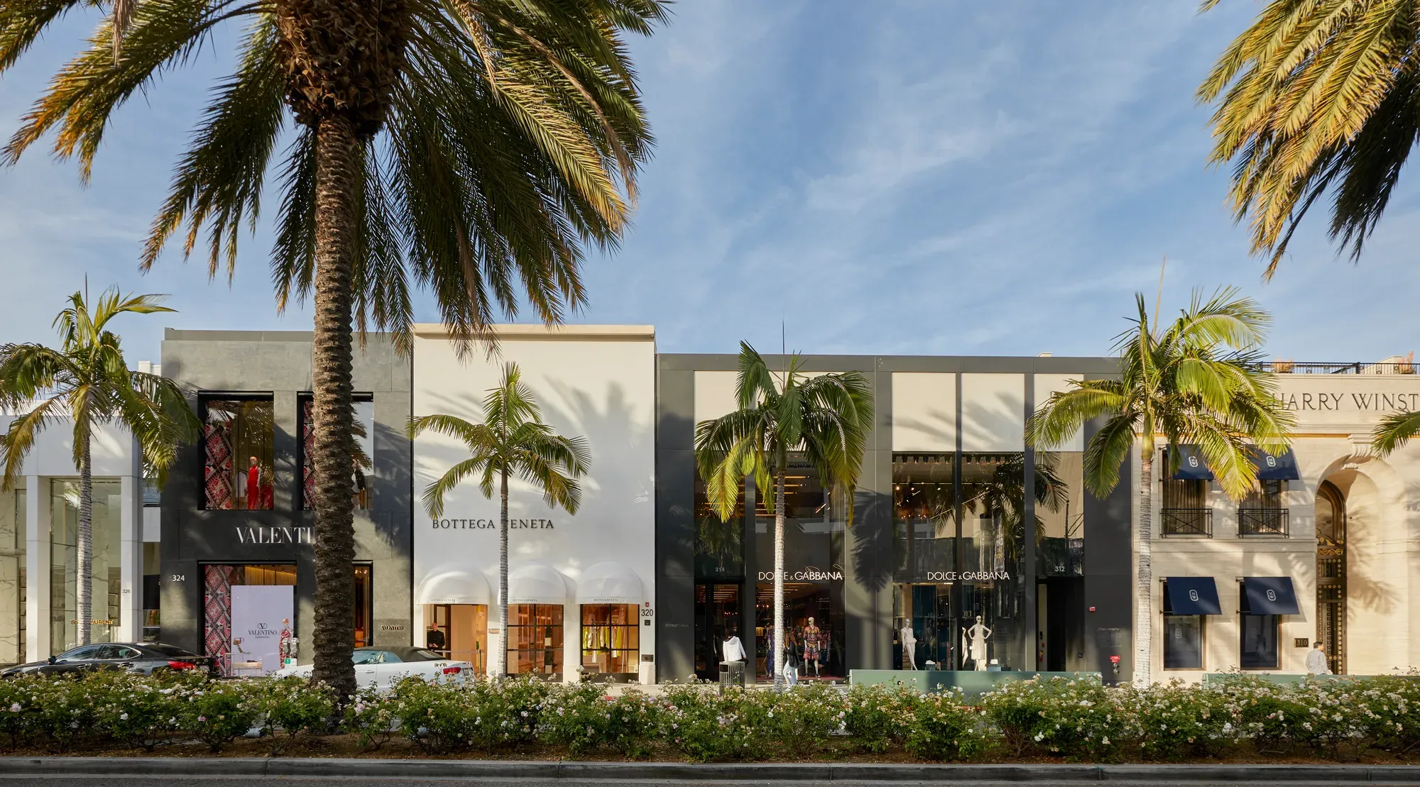 Rodeo Drive luxury storefronts—Valentino, Bottega Veneta, and Dolce & Gabbana—beneath tall palms and blue sky.