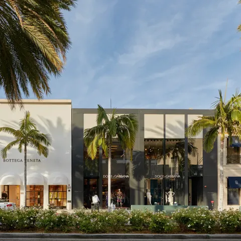 Rodeo Drive luxury storefronts—Valentino, Bottega Veneta, and Dolce & Gabbana—beneath tall palms and blue sky.