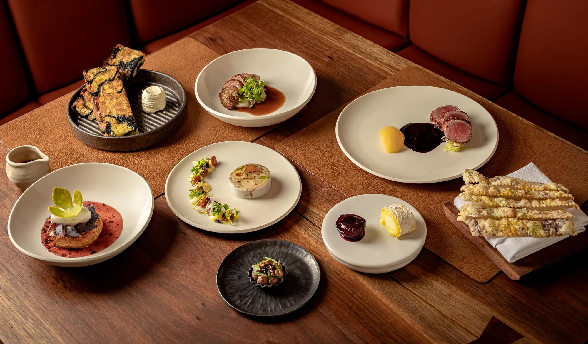 Assorted fine-dining dishes elegantly plated on white ceramics across a wooden restaurant table.