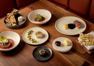 Assorted fine-dining dishes elegantly plated on white ceramics across a wooden restaurant table.