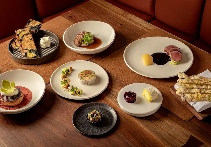 Assorted fine-dining dishes elegantly plated on white ceramics across a wooden restaurant table.