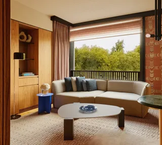 Modern living room with a neutral sectional sofa, blue and gray pillows, large window overlooking green trees.