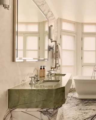 Luxurious marble bathroom featuring a freestanding white bathtub in front of frosted bay windows, with a double green marble vanity and large wall mirror on the left.