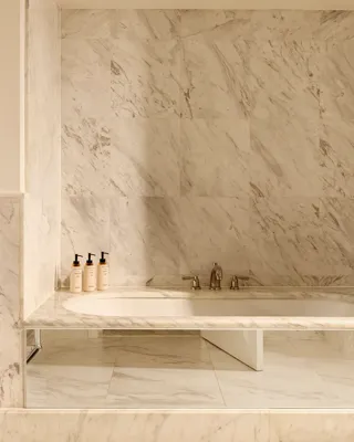  Bathroom in white marble with a built-in bathtub, chrome fixtures, and luxury toiletries displayed on the ledge.