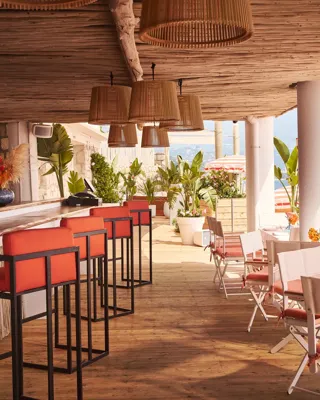 Terrasse ombragée avec tabourets corail, tables dressées et parasols rayés surplombant la mer