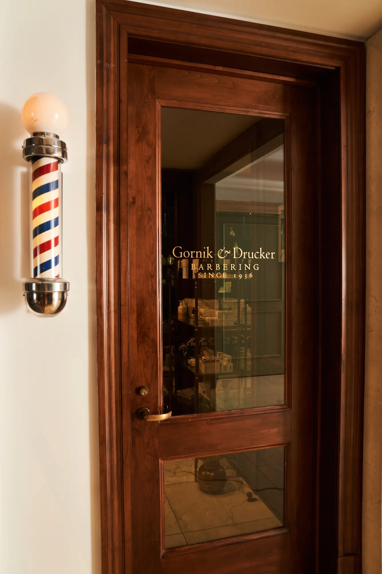 Entrance door with a gold decal on it leading into a traditional barbershop.