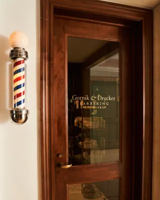 Entrance door with a gold decal on it leading into a traditional barbershop.