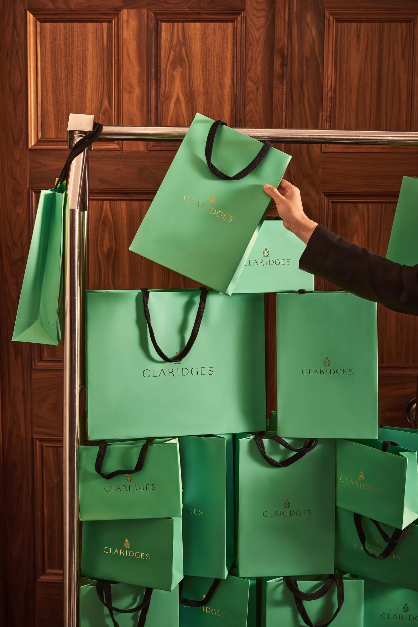 Claridge’s shopping bags displayed on a luggage trolley in front of wood-panelled doors.