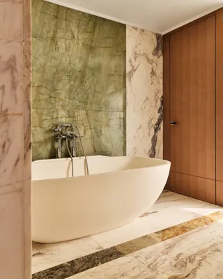 Elegant bathroom with freestanding oval bathtub, marble flooring, and green onyx accent wall beside wooden door.