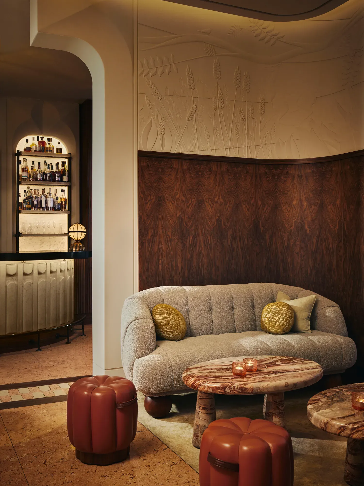 Cozy lounge area with a curved sofa, marble tables, and warm lighting, with a backlit bar visible in the background.
