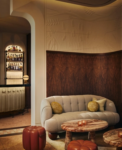 Cozy lounge area with a curved sofa, marble tables, and warm lighting, with a backlit bar visible in the background.