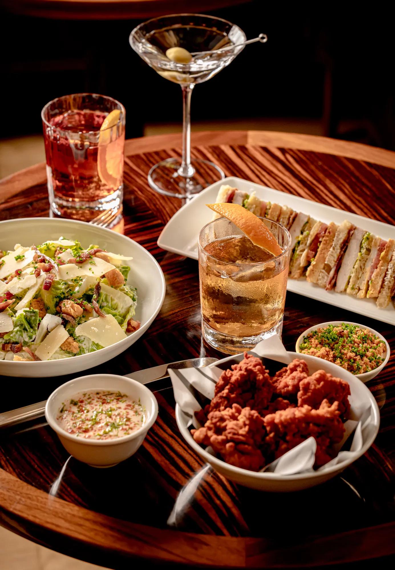 Copilot said:

Selection of cocktails, fried chicken, sandwiches and salad served on a wooden table.