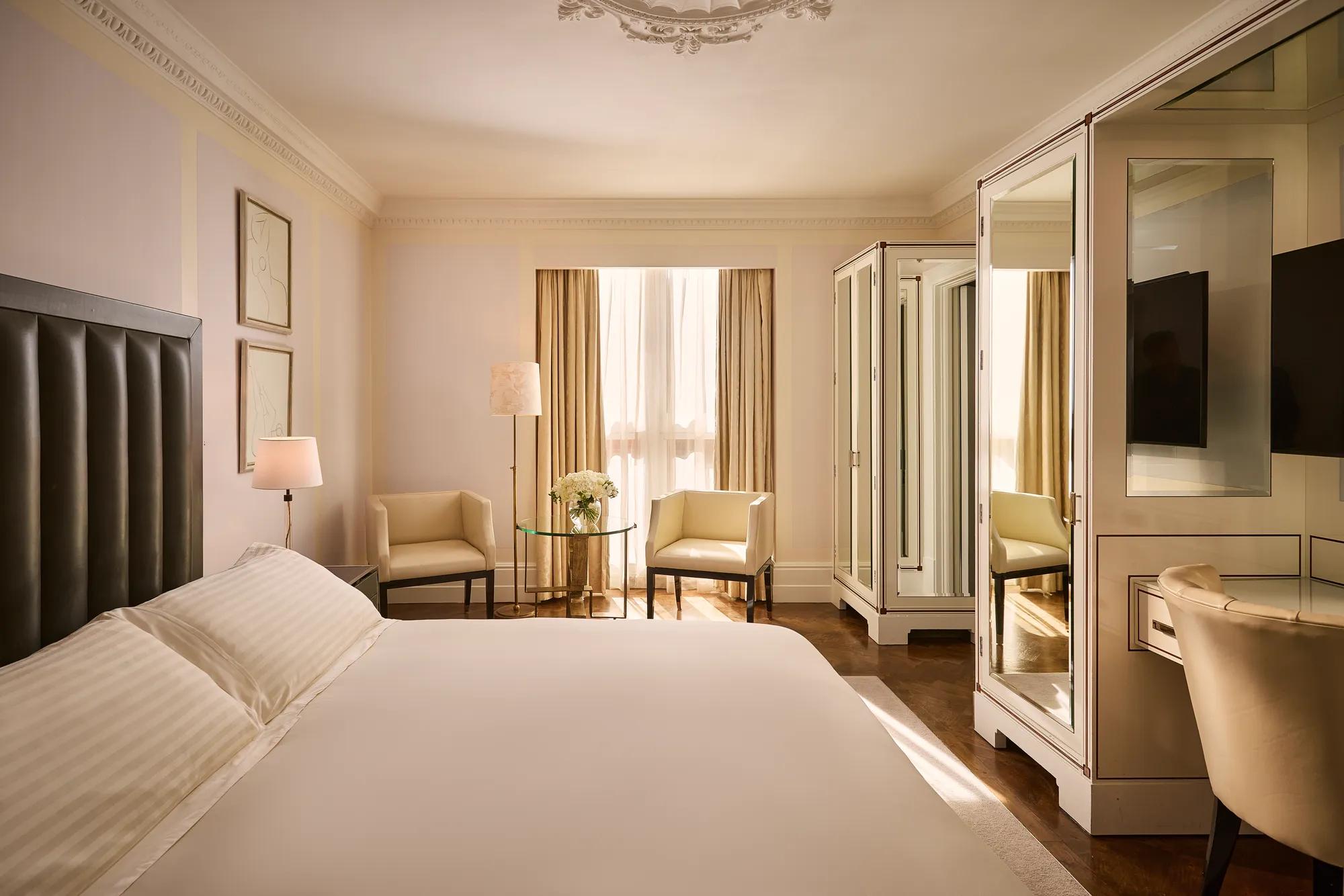 **Alt text:**
Elegant bedroom with a king-size bed, mirrored wardrobes, seating area by the window, walnut floors and a writing desk.
