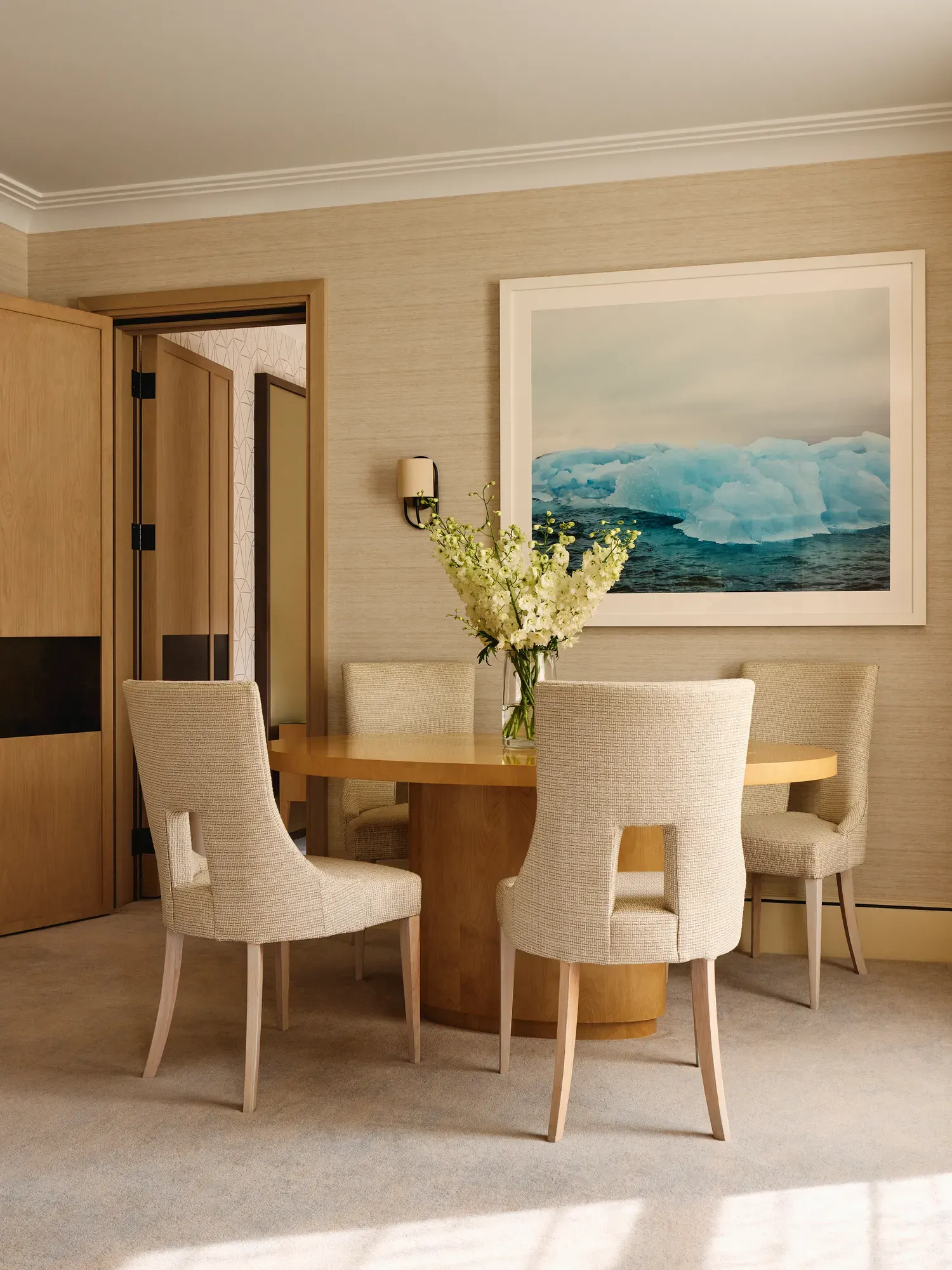 Intimate dining space with a circular wooden table and upholstered chairs, accented by a framed photograph of blue icebergs.