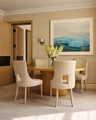 Intimate dining space with a circular wooden table and upholstered chairs, accented by a framed photograph of blue icebergs.