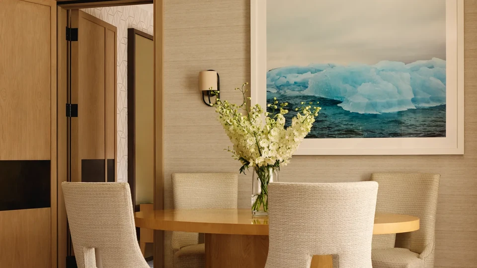 Intimate dining space with a circular wooden table and upholstered chairs, accented by a framed photograph of blue icebergs.
