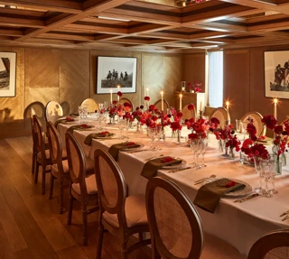 Intimate dining room with a long table set with red floral centerpieces and candles under a mirrored coffered ceiling.